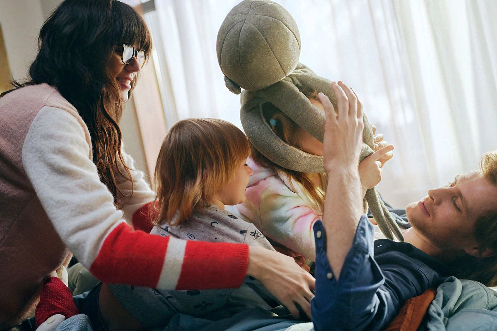 Familienzeit im Wohnzimmer: Fröhliches Spiel mit Kuscheltier im Sonnenlicht.