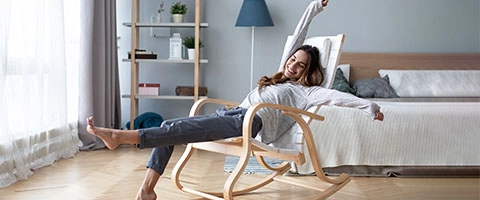 Entspannte Frau im Schaukelstuhl, modernes Schlafzimmer, Wohlfühlatmosphäre.