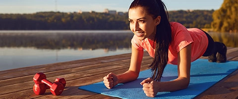Fitness-Enthusiastin beim Plank-Workout am See für effektives Ganzkörpertraining.