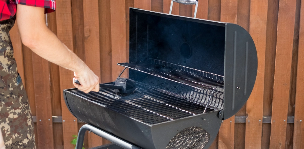 Mann reinigt Grillrost mit Grillbürste