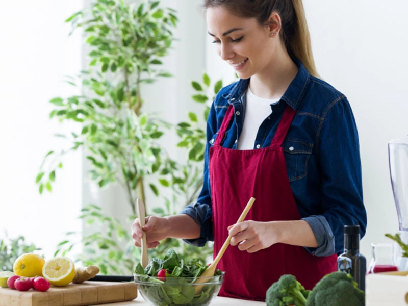 Fröhliche Frau bereitet gesunden Salat zu, frische Zutaten, gesunde Ernährung.
