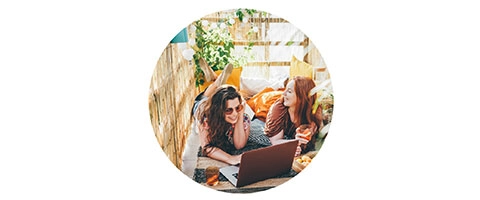 Gemütliche Sommerterrasse: Zwei Frauen genießen Drinks und Laptop im Freien.