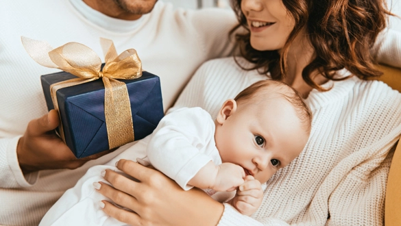 Ein Paar hält sein Neugeborenes und ein Geschenk im Arm