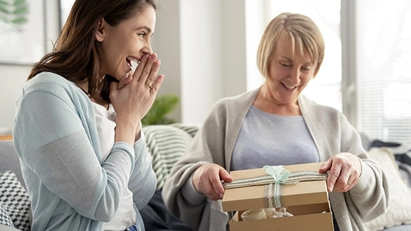 Eine Frau freut sich, während die Beschenkte das Geschenk auspackt