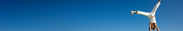 Dynamischer Handstand im Freien vor strahlend blauem Himmel und grüner Wiese.