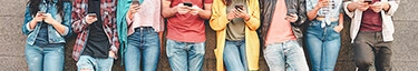 Junge Menschen mit Smartphones, lässig an einer Wand lehnend, vernetzt und trendbewusst.