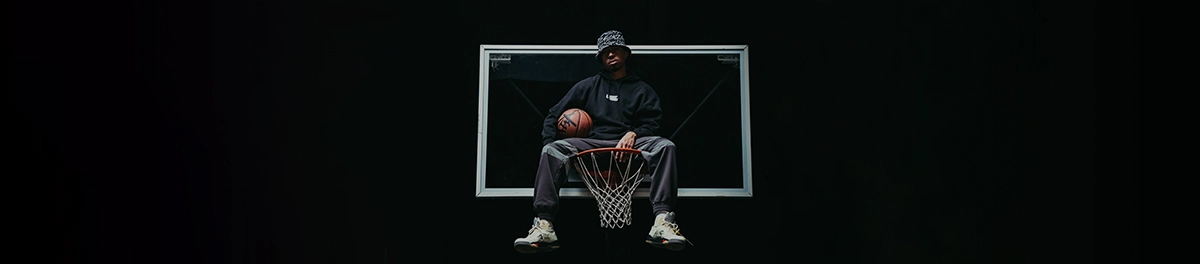 Basketballspieler sitzt lässig auf Korb, urbaner Stil, dynamische Sportfotografie.