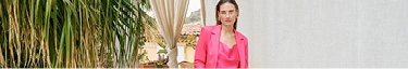 Elegante Frau im pinken Anzug vor mediterraner Kulisse, stilvoll und modern.