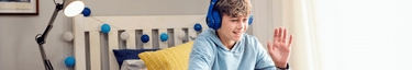 Junger Gamer mit blauen Kopfhörern, lächelnd am Schreibtisch, in modernem Kinderzimmer.