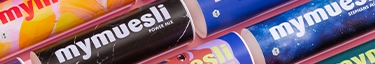Bunte Müsliverpackungen von mymuesli auf rosa Hintergrund, Vielfalt und Genuss entdecken.