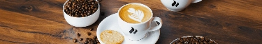 Köstlicher Cappuccino mit Latte Art, umgeben von frischen Kaffeebohnen auf Holztisch.